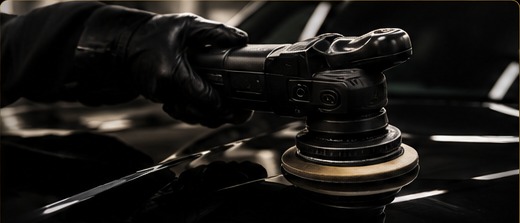 Professional dual-action machine polisher correcting black car paintwork